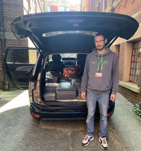 A man stands next to a vehicle with the tailgate open to show the car full of laptops