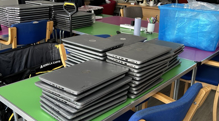 Green and pink tables with laptops stacked up on them